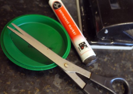 A recycled plastic lid next to scissors.