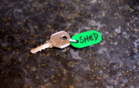 A key with a green plastic fob that says "SHED".