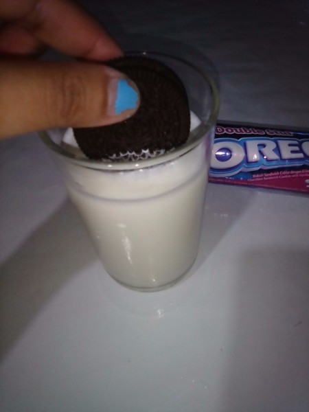 An Oreo cookie being dunked into a glass of milk.