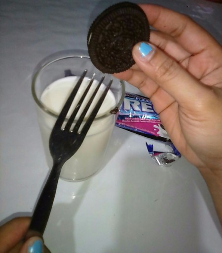 An Oreo cookie placed on a fork, next to a glass of milk.