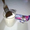 An Oreo cookie placed on a fork, being dipped into a glass of milk.