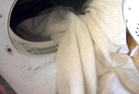 A white towel being placed in an open dryer.