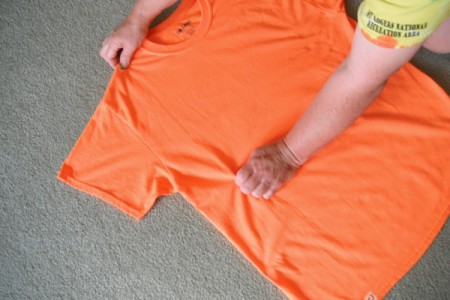 Folding an orange T-shirt.