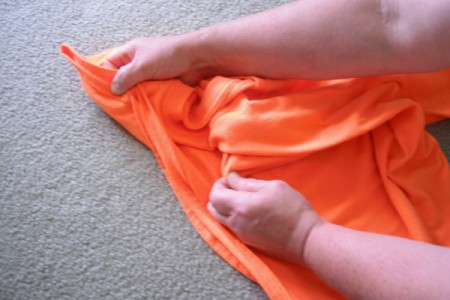 Folding an orange T-shirt.