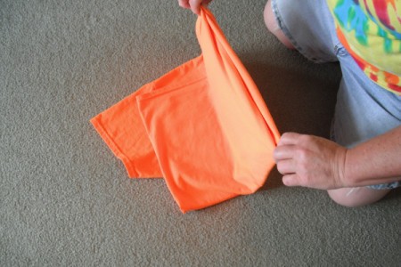 Folding an orange T-shirt.