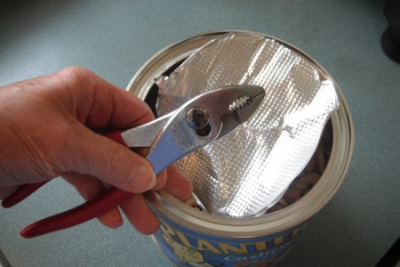 A pair of pliers being used to remove the seal from a container of food.
