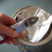 A pair of pliers being used to remove the seal from a container of food.