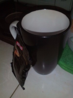An empty mug next to a sachet of instant coffee.