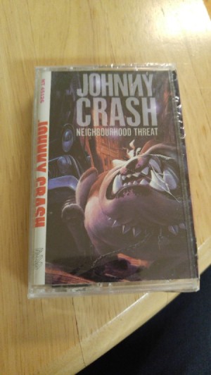 A sealed Johnny Crash "Neighborhood Threat" cassette tape, still sealed in plastic.