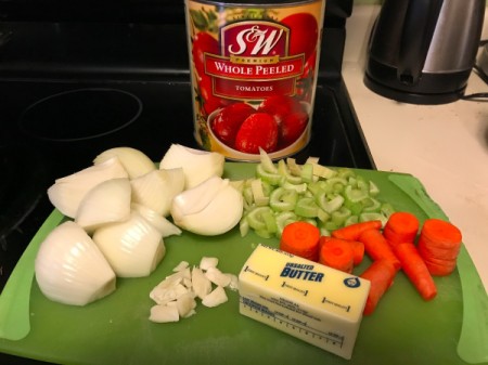 A large can of tomatoes with chopped vegetables, ready to be made into soup.