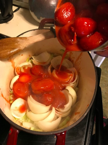 Pouring a can of tomatoes into a soup pot.