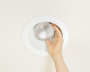 A hand trying to remove a bulb from a recessed light fixture.