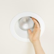 A hand trying to remove a bulb from a recessed light fixture.