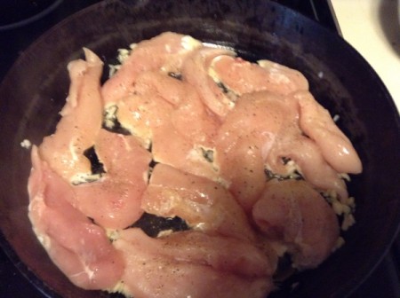 Chicken breast being browned in a large cast iron frying pan.