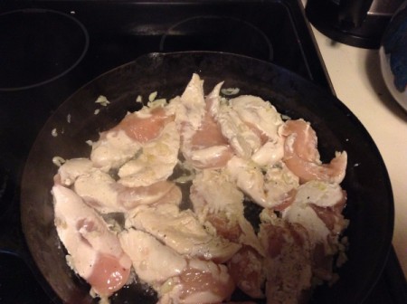 Chicken breast being browned in a large cast iron frying pan.