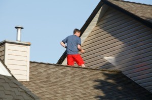 A man standing on a roof cleaning his home's siding with a pressure washer.