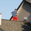 A man standing on a roof cleaning his home's siding with a pressure washer.