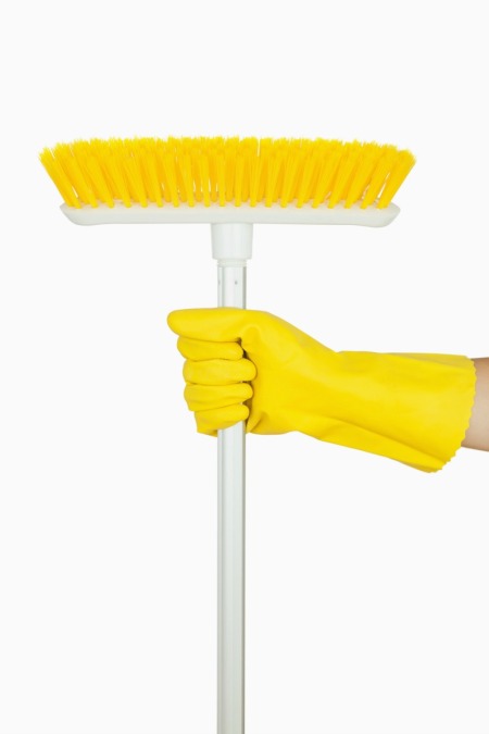 A yellow broom with white handle being held by a hand wearing a rubber cleaning glove.