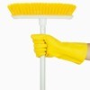 A yellow broom with white handle being held by a hand wearing a rubber cleaning glove.