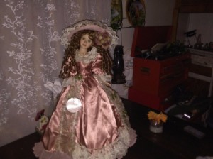 A doll wearing an old fashioned satin dress and large hat.