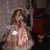 A doll wearing an old fashioned satin dress and large hat.