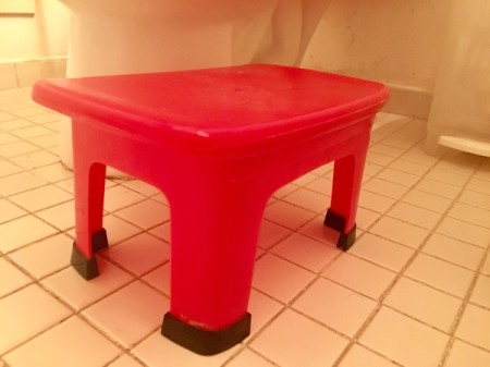 A red stepstool next to a toilet.