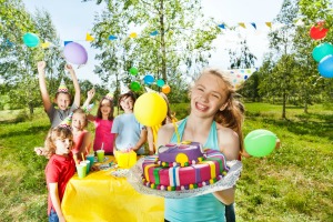 A 12 year old girl smiling and holding a birthday cake at an outdoor birthday party.