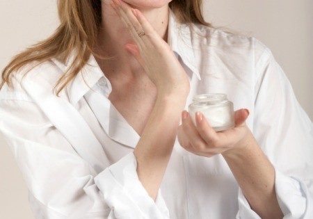 A woman applying cream to her neck.