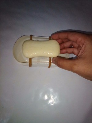 Two rubber bands holding a bar of soap over a soap dish.
