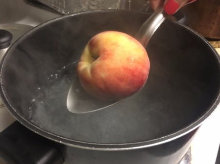Placing a peach in a pot of boiling water to remove the skin.
