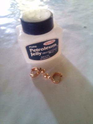 A gold colored earring next to a jar of petroleum jelly.