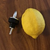 An oil bottle dispenser next to a lemon.