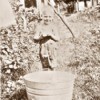 A sepia photograph of a young boy with a metal tub outside.