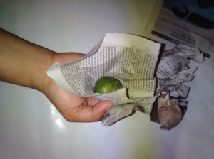 A lemon being wrapped in newspaper for storage.