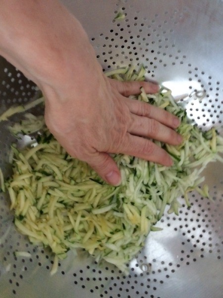 squeezing juice from shredded Zucchini in colander