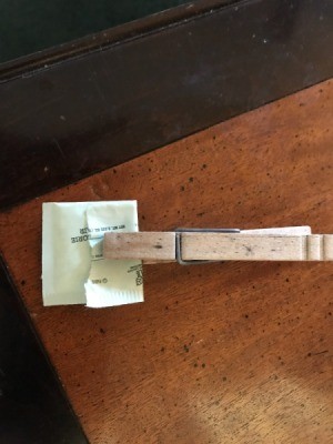 A clothespin holding a single serving packet of sweetener closed.