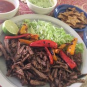 Skillet Carne Asada on plate with peppers lime and cabbage