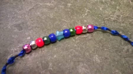 Beads strung onto the center of a length of blue ribbon.