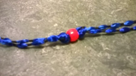 A red bead is threaded onto both strands and a knot tied behind it.