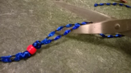 Cutting the blue ribbon, with a red bead tied to the end.