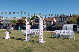 An arbor and white chairs set up outdoors for a wedding.