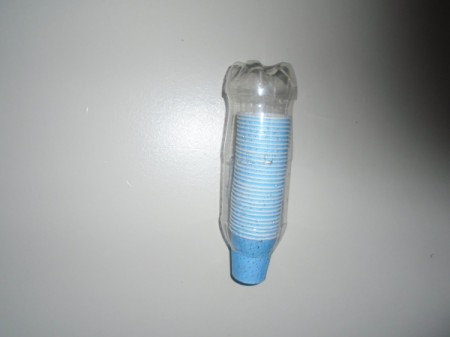 A plastic soda bottle cut to be used for storing small paper cups in the bathroom.