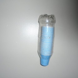 A plastic soda bottle cut to be used for storing small paper cups in the bathroom.