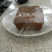 A piece of zucchini bread on a plate, covered in plastic wrap.