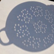 A colander showing crescent moon shaped shadows on a light surface, from the solar eclipse.