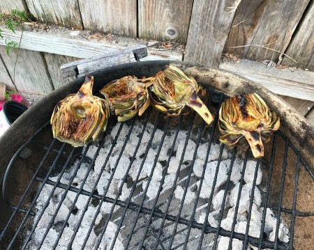 Artichoke halves on the outside edge of a round charcoal grill.