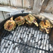 Artichoke halves on the outside edge of a round charcoal grill.