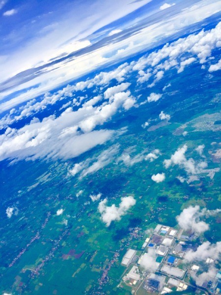 A view from above the clouds, looking down at the green land and buildings.