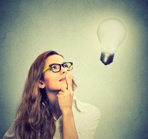 A woman in glasses looking up at a lightbulb.