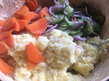 adding carrots, cucumbers and onion to potatoes
